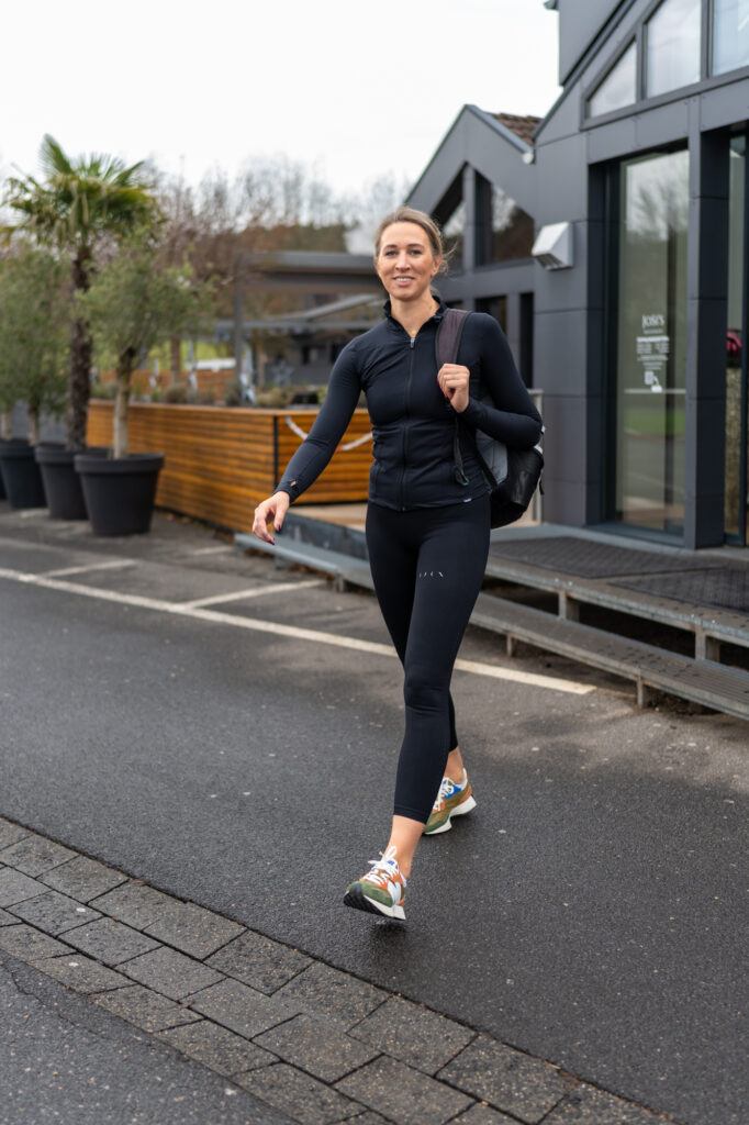 Frau in schwarzer Sportkleidung geht auf einem Weg vor einem Gebaeude